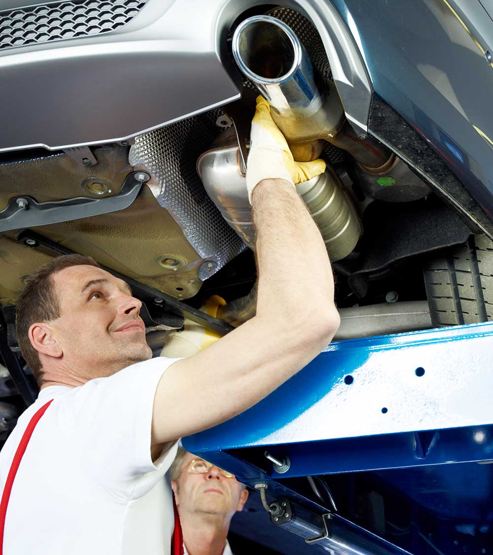 Zwei Kfz-Mechaniker reparieren die Abgasanlage eines Autos