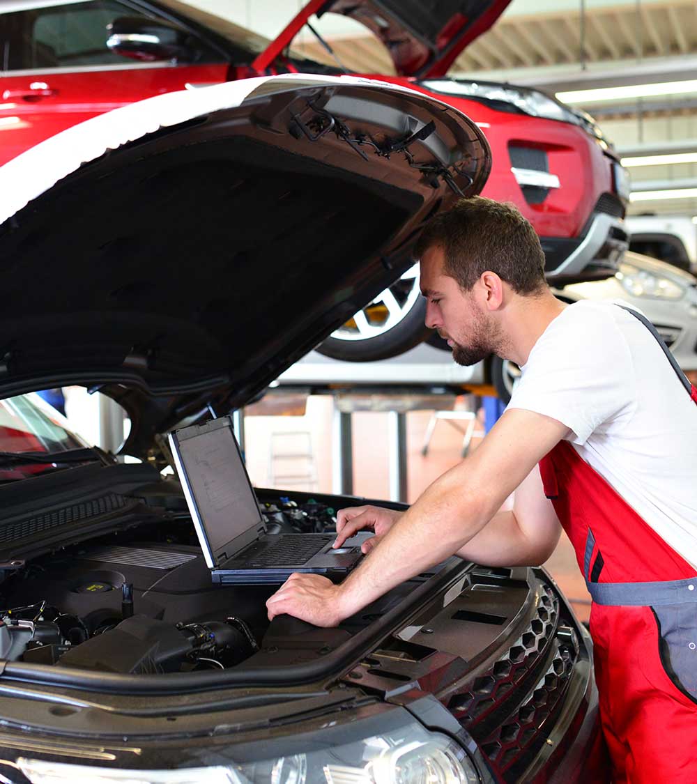 KFZ Mechaniker mit Diagnosegerät am Motor eines Fahrzeuges